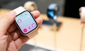 Une main tient une montre connectée affichant l'heure 20:06, des indicateurs d'activité et le logo watchOS 26.