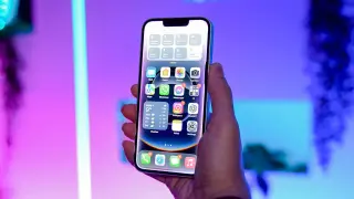 Main d'une personne tenant un iPhone affichant iOS 26.3, avec des widgets météo et des icônes d'applications.