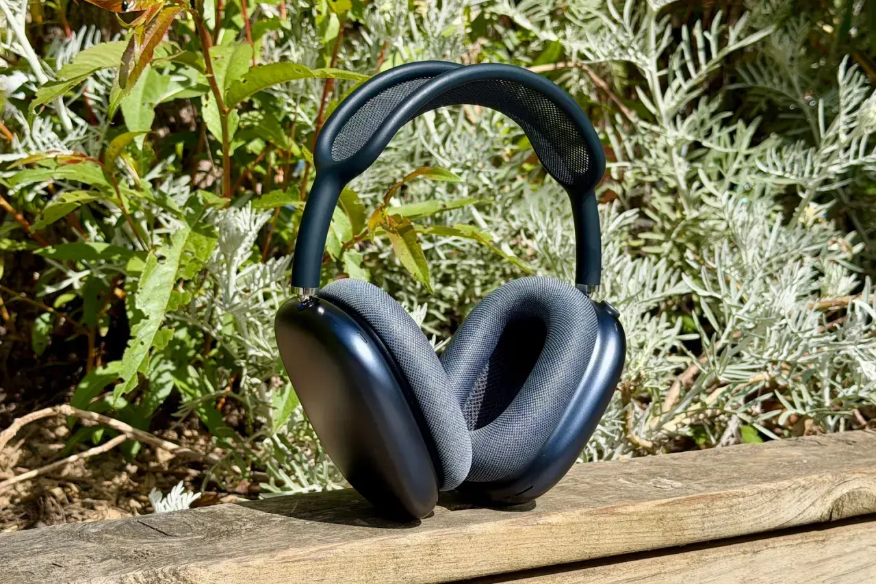 Casque AirPods Max 2 bleu nuit, posé sur un banc en bois, entouré de verdure.