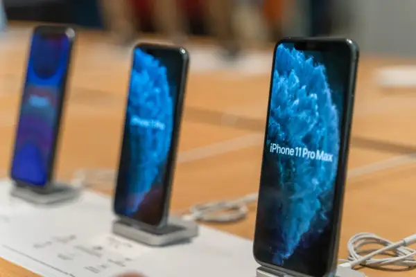 Trois iPhone 11 Pro Max sont alignés sur un présentoir, affichant un fond d'écran bleu abstrait.